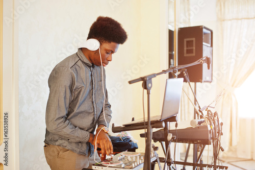 African american dj in huge white headphones creating music on mixing panel. © AS Photo Family