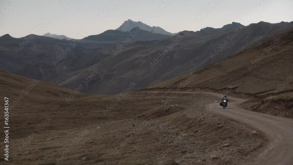 Man in motorcycle passing the road inside the Andean Mountains on the background the snowy peaks. Andean landmark. Man in motorcycle passing the road inside the Andean Mountains on the background the snowy peaks. Andean landmark.