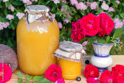 Golden honey in glass jar and colorful flowers.