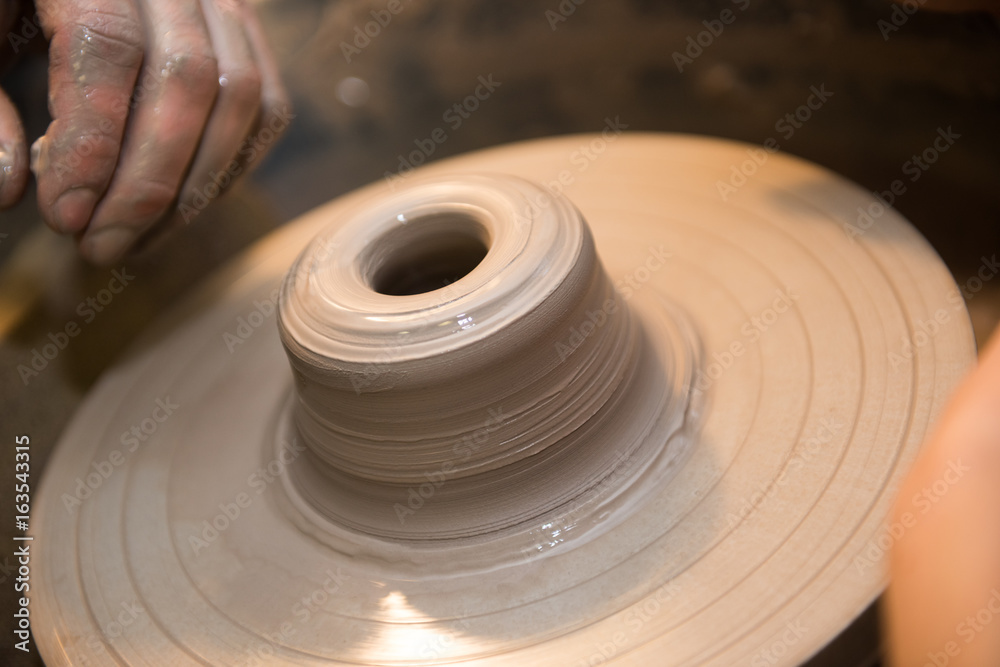 Obraz premium Hands working on a spinning pottery wheel, making pottery out of clay mud. close up photograph with a shallow depth of field.