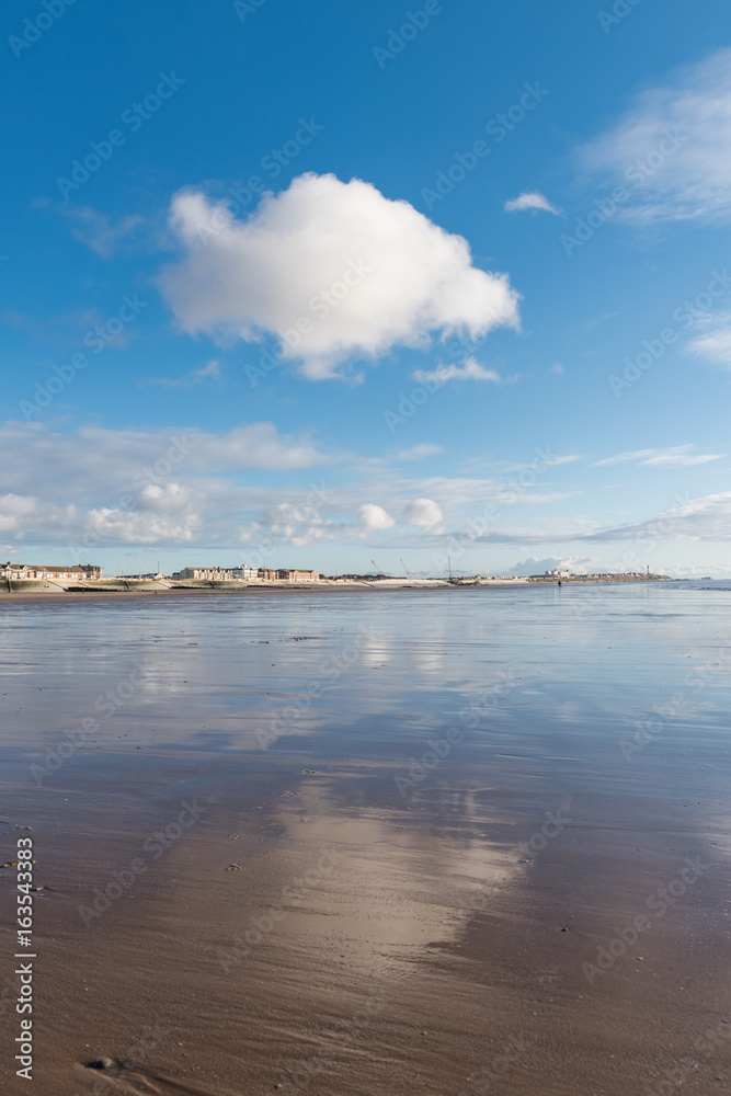 Beautiful blue sky and textured sand, on a cool sunny winters day at the beach. The clouds reflect off the wet sand.