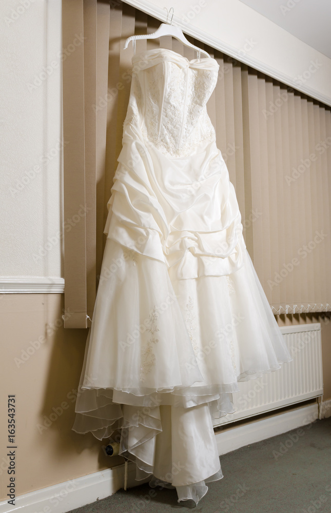 A beautiful cream and clean Wedding dress Hanging in front of a Window in a hotel room. A beautiful cream and clean Wedding dress Hanging in front of a Window in a hotel room.