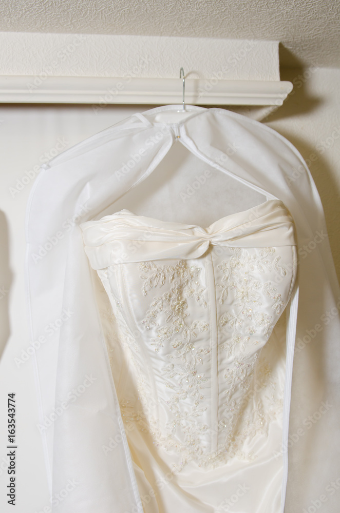 A beautiful cream and clean Wedding dress Hanging in front of a Window in a hotel room. A beautiful cream and clean Wedding dress Hanging in front of a Window in a hotel room.