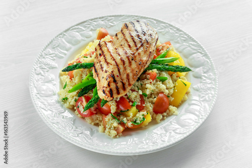 couscous salad with grilled chicken and asparagus on white plate. wooden table. healthy food