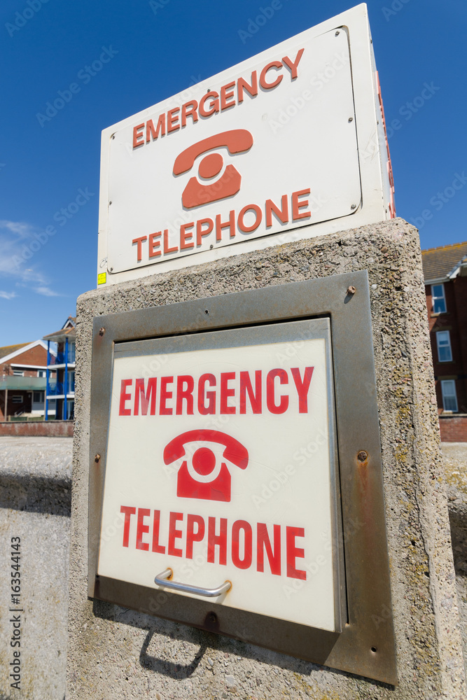 An retro old weathered and distressed emergency telephone sign, on a rustic seaside wall near the ocean and swimmers. The sign is old and vintage. An retro old weathered and distressed emergency telephone sign, on a rustic seaside wall near the ocean and swimmers. The sign is old and vintage.