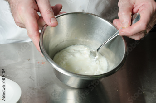 Thick fresh sweet dessert cream, being mixed and whisked in a metal container in an industrial kitchen.