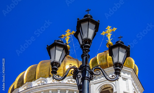 Black carved lantern with crosses on the background of the golden domes of the Russian Orthodox Church and blue monophonic sky 