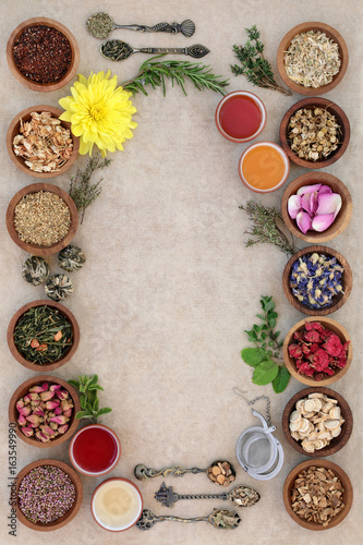 Herb tea selection forming an abstract background with strainer, oriental tea cups and old spoons on natural hemp paper. Teas used in natural alternative medicine.