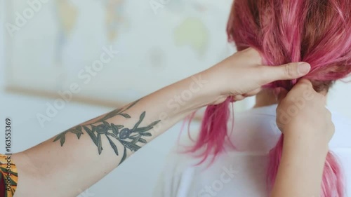 Hand held shot of young authentic hipster millennial girl with tattoos doing a braid to her friend a young woman with rose pink unconventional hair style, concept friendship, special and original photo