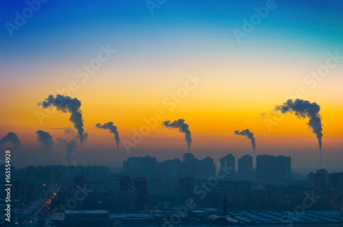 Evening view of the industrial landscape of the city with smoke emissions from chimneys at sunset