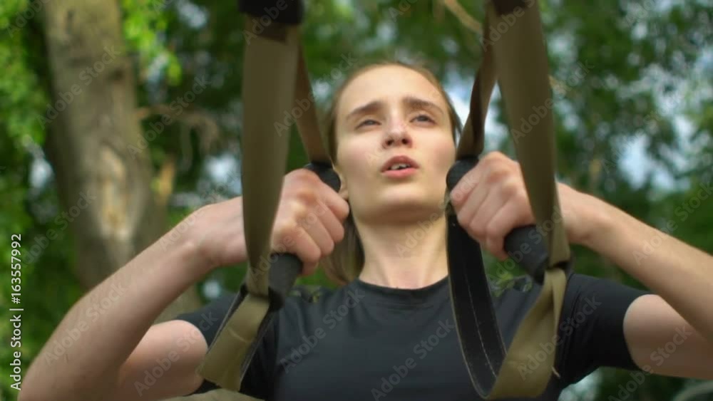 Attractive young woman doing exercises with trx outdoors