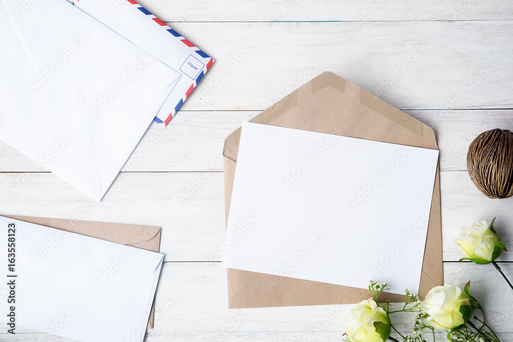Top view of envelope and blank greeting card with rose flowers on white wooden background. Top view of envelope and blank greeting card with rose flowers on white wooden background.