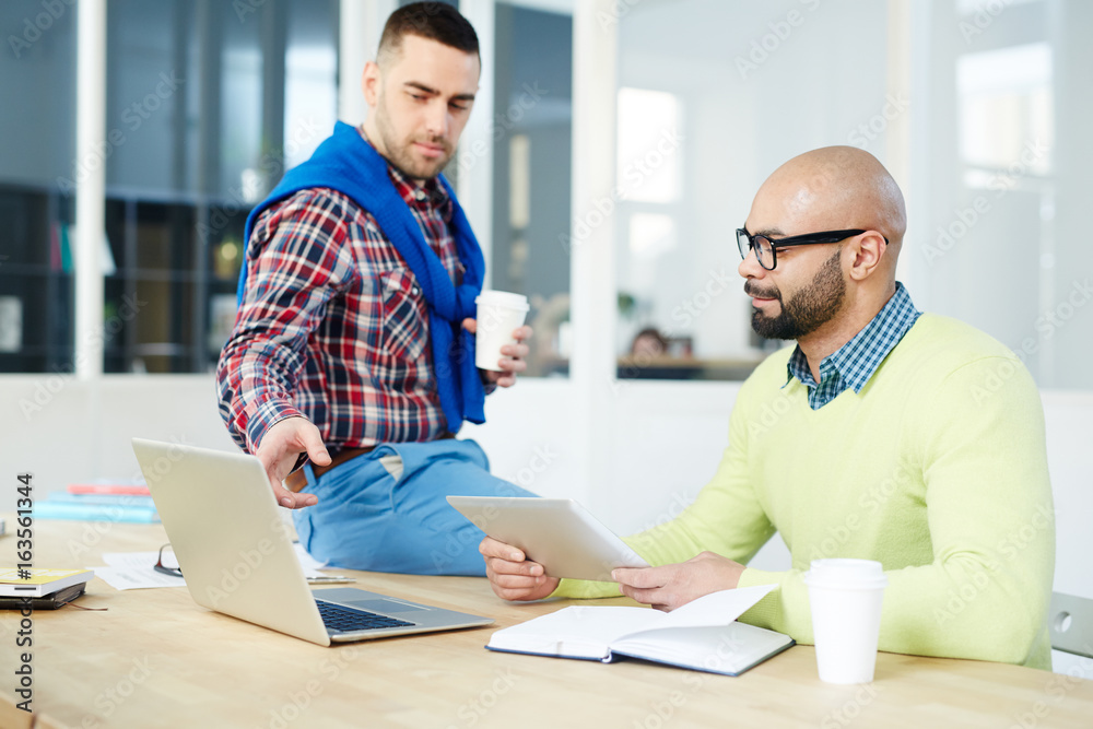 Confient man pointing at laptop display while explaining data to colleague with touchpad Confient man pointing at laptop display while explaining data to colleague with touchpad