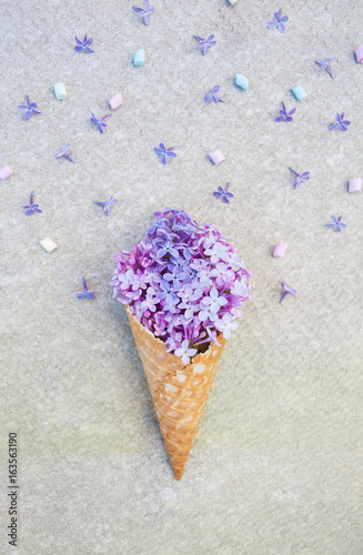 Ice cream of lilac flowers in waffle cone on light gray stone background from above, beautiful floral arrangement, floral composition, flat lay