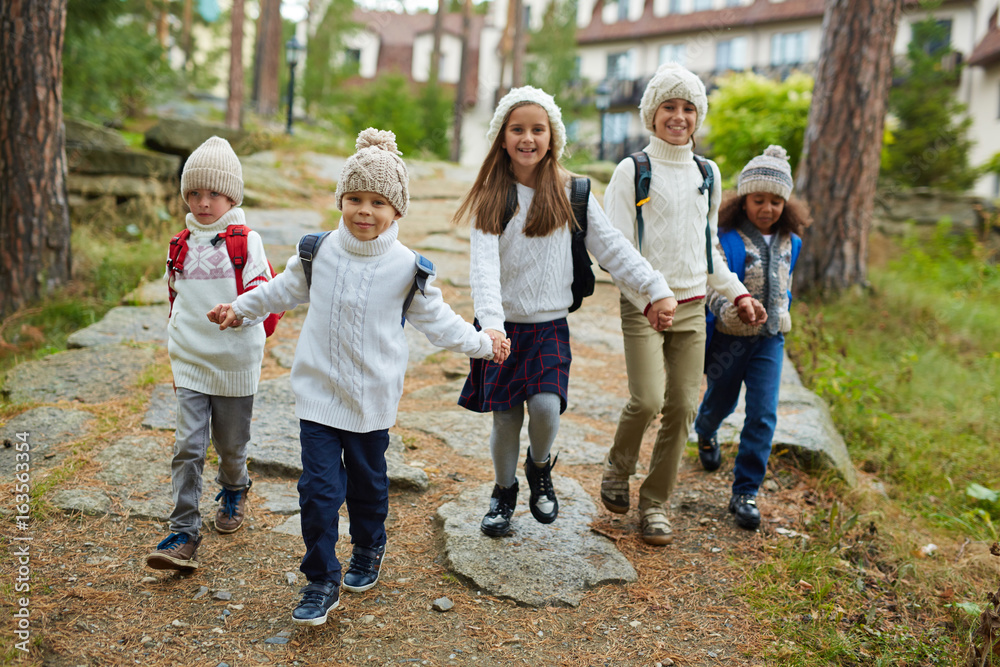 Fototapeta premium Group of cheerful children running towards camera holding hands on their first school day in September