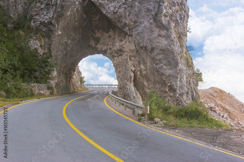 Asphalted mountain road with sharp sharp turn near the cliff. Tunnel in the rock or hole in the rock cave