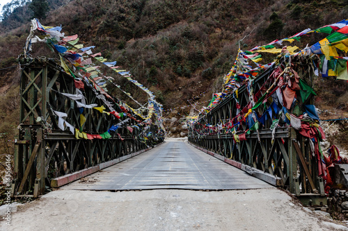 Tibetan prayer flags swaddled with bridge over frozen river with Black mountain with snow on the top is background at Thangu and Chopta valley in winter in Lachen. North Sikkim, India. © artitwpd