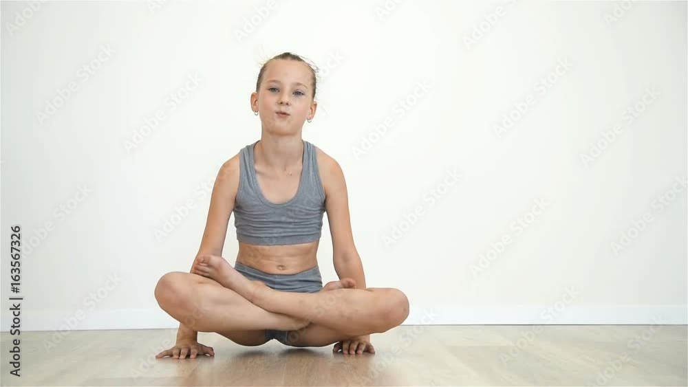 Little Girl Sitting On Floor In Lotus Position. Slow Motion Effect Little Girl Sitting On Floor In Lotus Position. Slow Motion Effect
