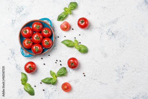 Fresh cherry tomatoes on a plate, basil leaves and black pepper on stone table, top view