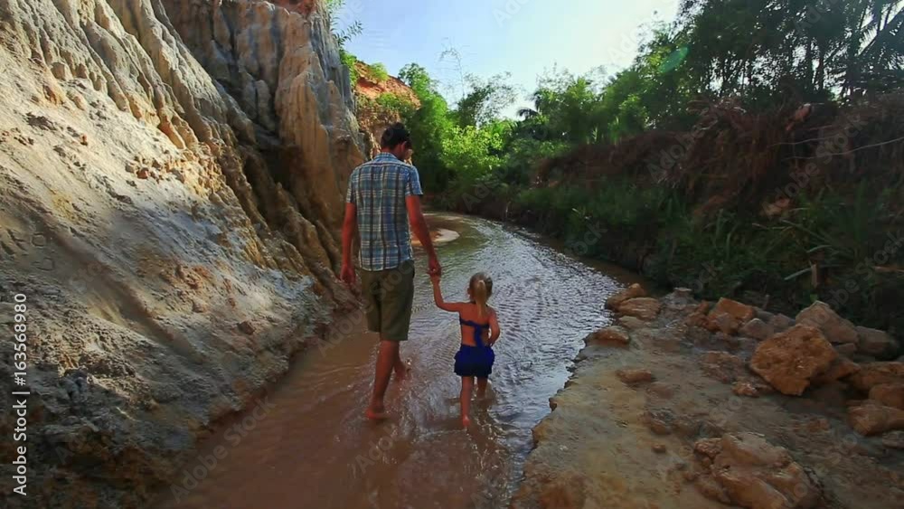 Backside view dad with little daughter with pigtail in blue swimsuit walk between shady Fairy Stream banks in Vietnam Backside view dad with little daughter with pigtail in blue swimsuit walk between shady Fairy Stream banks in Vietnam