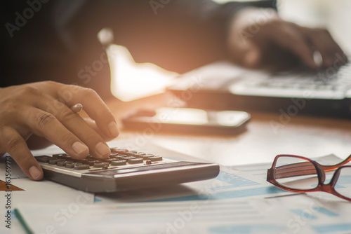 A businessman analyzing investment charts at his workplace and using his laptop and touch calculator.