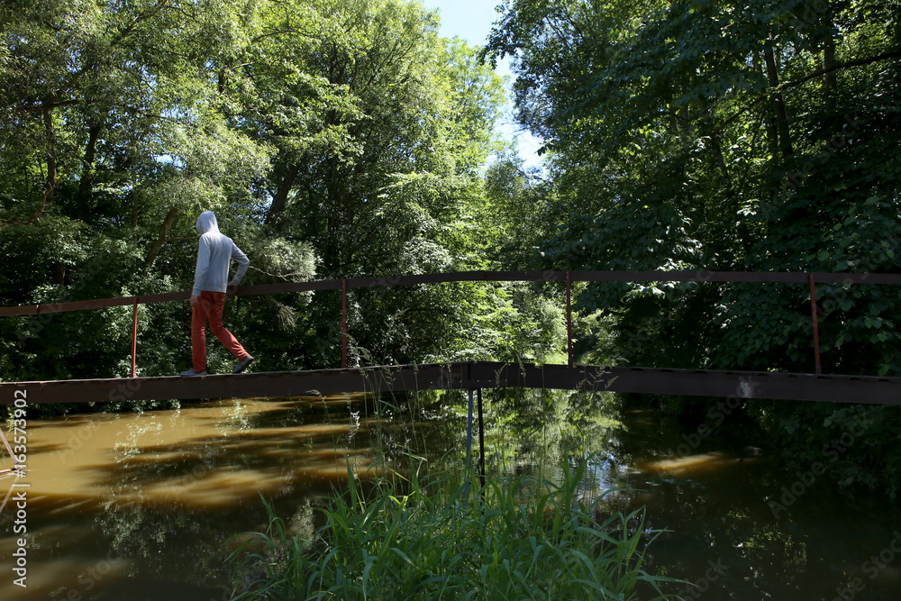 Man walking on wooden bridge over the river with lush green foliage.  The river Jiesia in Lithuania, East Europe.