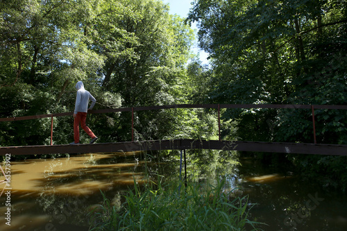Man walking on wooden bridge over the river with lush green foliage. The river Jiesia in Lithuania, East Europe.