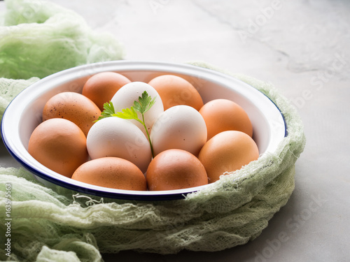 White and brown hen eggs in bowl on concrete gray background