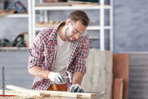 Carpenter driving nail into wooden plank in light workshop