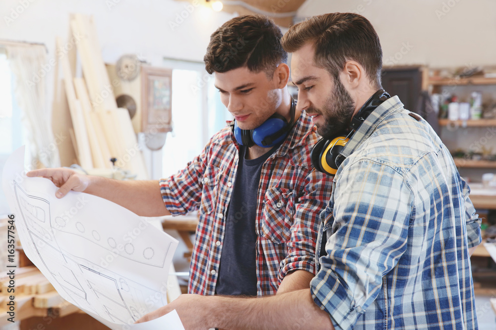 Two handsome young carpenters with drawing in workshop Two handsome young carpenters with drawing in workshop