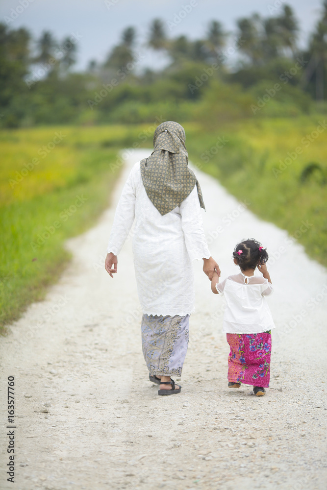 Obraz premium Mom holding her baby girl hand with hari raya dress
