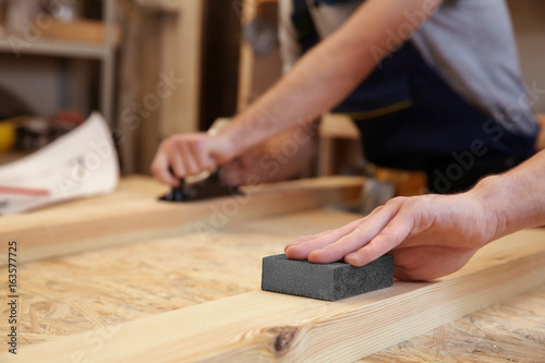 Hand of carpenter machining wooden board with abrasive stone, closeup