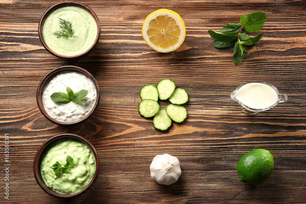 Delicious yogurt sauces in bowls with ingredients on wooden table Delicious yogurt sauces in bowls with ingredients on wooden table