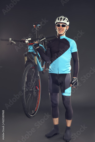 Young sporty cyclist with bicycle on dark background