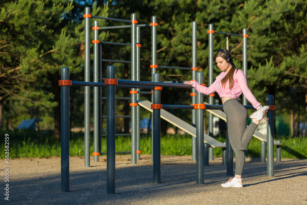 Fototapeta premium Young woman in earphones doing stretching exercises outdoor