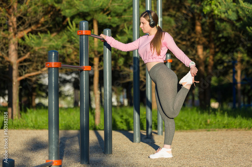 Young woman in earphones doing stretching exercises outdoor
