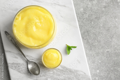 Glass jar with yummy lemon curd on white marble board photo