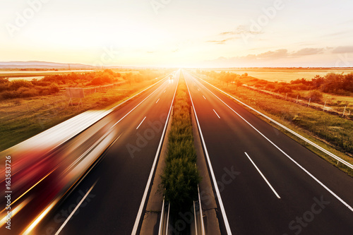 Highway landscape in a strong back light at sunset with motion blurred truck photo