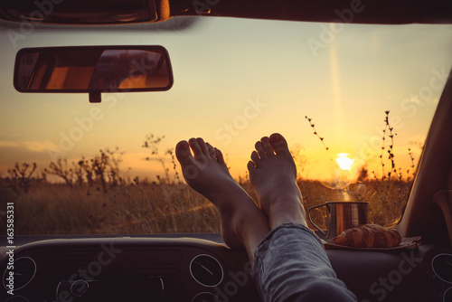 Woman feet on car dashboard. Drinking take away tea and сroissant .