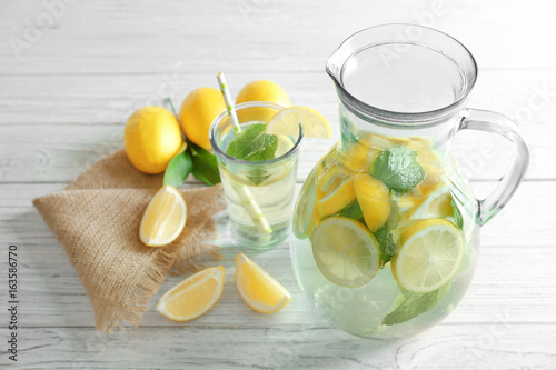 Jug and glass with refreshing lemon water on wooden table