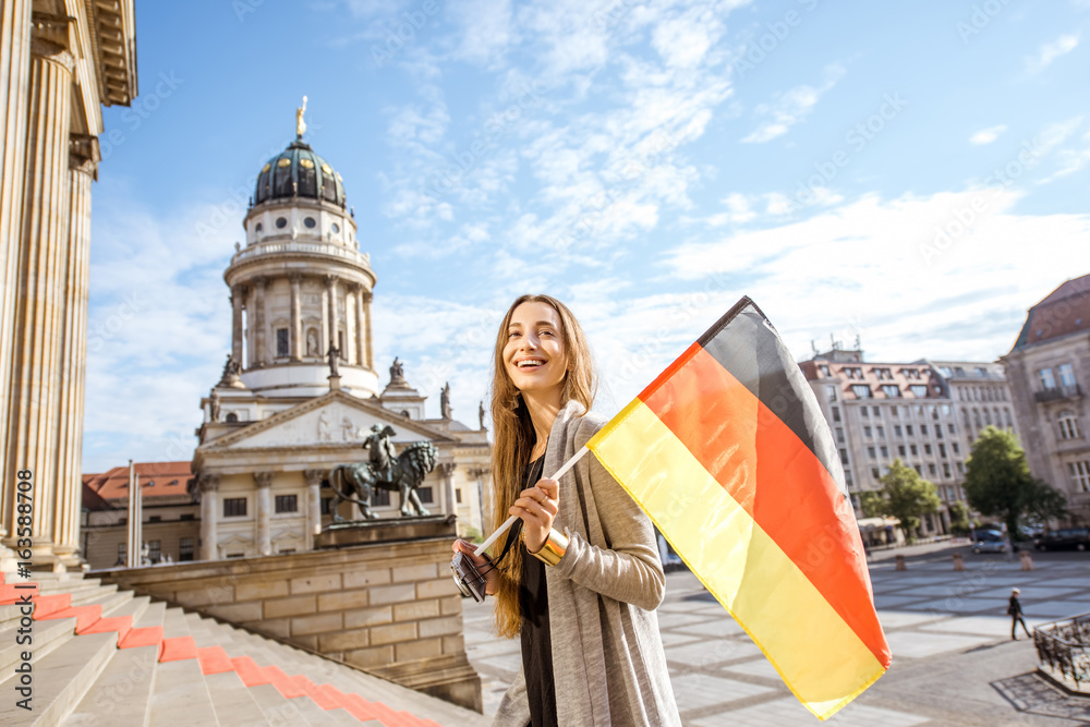 Fototapeta premium Turystyczna młoda kobieta spaceru z niemiecką flagą na schodach w pobliżu domu koncertowego w Berlinie