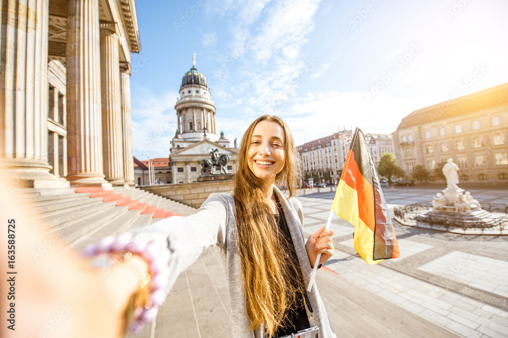 Young woman tourist making selfie photo standing with german flag on the stairs near the Concert house in Berlin