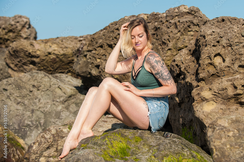 Beautiful women seductively seated on boulder rocks as she adjusts her blond hair. Beautiful women seductively seated on boulder rocks as she adjusts her blond hair.
