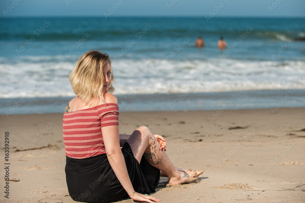 Beautiful short hair woman seated on beach sand peeking over shoulder. Beautiful short hair woman seated on beach sand peeking over shoulder.