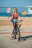 Blond beach girl on cruiser bike smiling on sunny beach cul de sac.