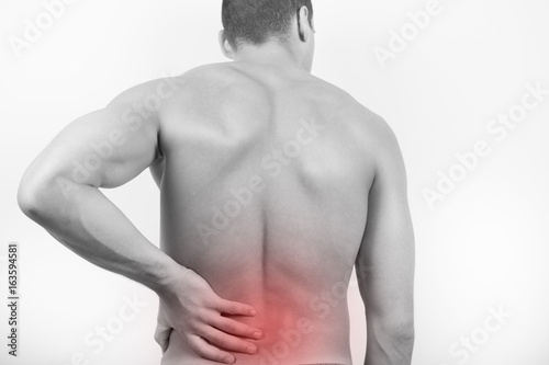 Rear view of a young man holding his back in pain, isolated on white background. Lower back pain. Shirtless man touching his back for the pain.