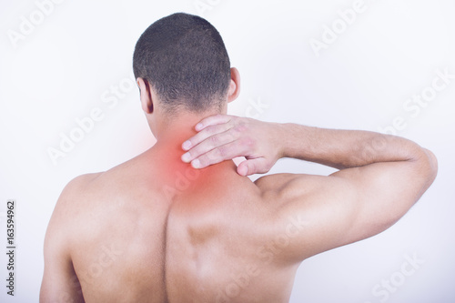 Rear view of a young man holding his neck in pain, isolated on white background. Lower neck pain. Shirtless man touching his neck for the pain.
