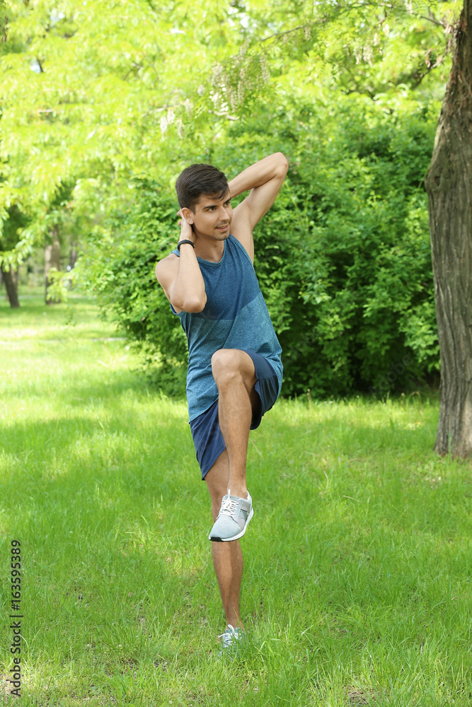 Athletic young man doing bicycle crunch exercise while standing on grass in green spring park Athletic young man doing bicycle crunch exercise while standing on grass in green spring park