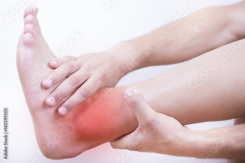 Close up view of a young man holding his ankle in pain, isolated on white background. Lower leg pain. Young man touching his ankle for the pain. Red inflammation effect.