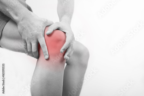 Close up view of a young man holding his knee in pain, isolated on white background. Knee and leg pain. Young man touching his knee for the pain. Red inflammation effect.
